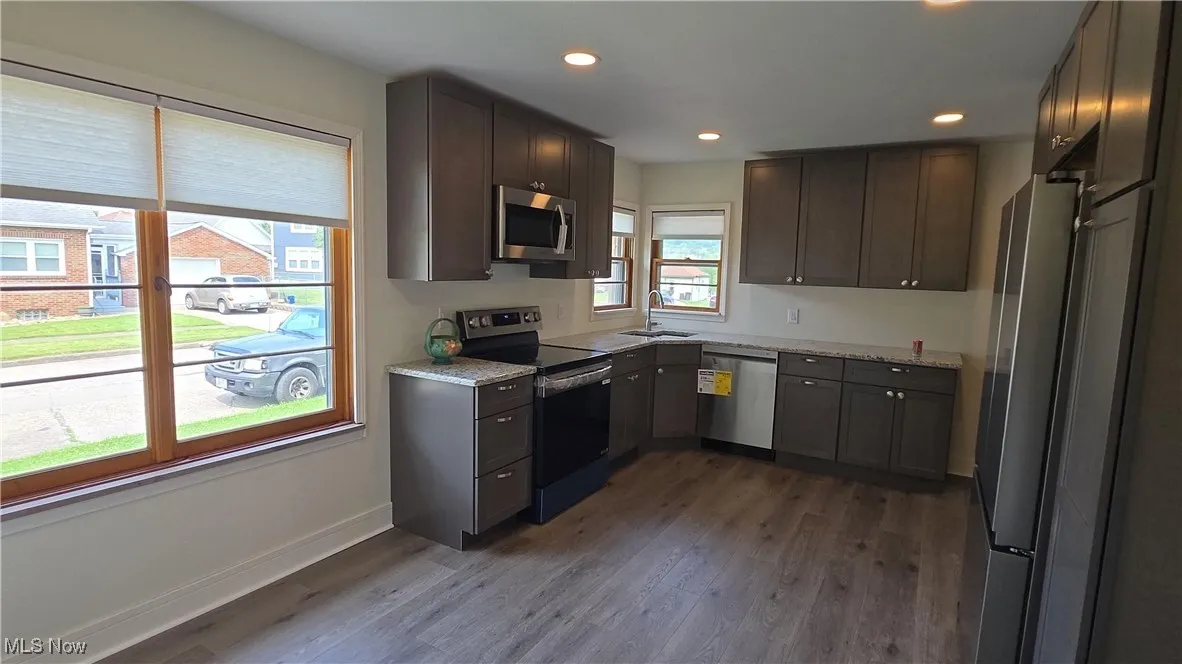 Kitchen with appliances with stainless steel finishes, dark wood-type flooring, recessed lighting, light stone countertops, and dark brown cabinets