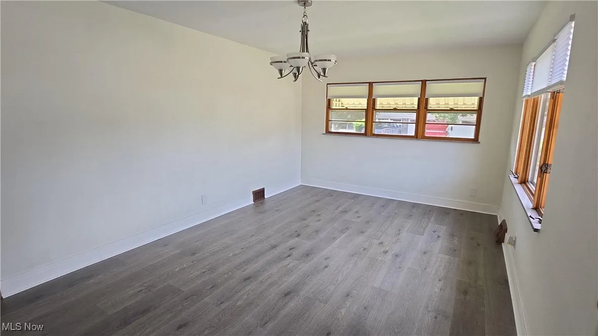 Unfurnished dining area featuring a chandelier, plenty of natural light, and dark wood-type flooring