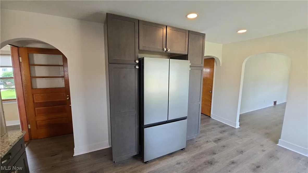 Kitchen featuring arched walkways, freestanding refrigerator, light wood-style floors, recessed lighting, and light stone countertops