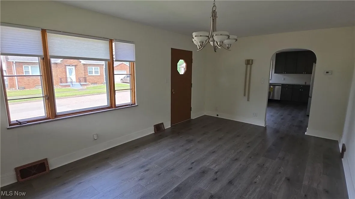Unfurnished dining area featuring arched walkways, dark wood-style flooring, and a chandelier