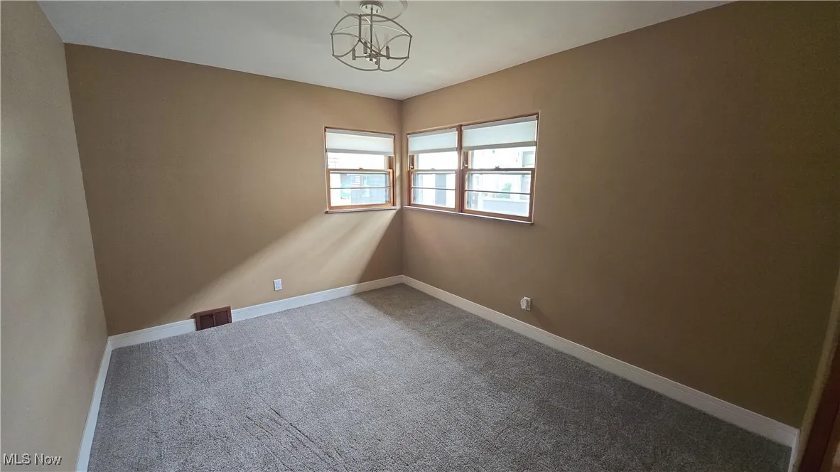 Carpeted empty room with a chandelier and baseboards