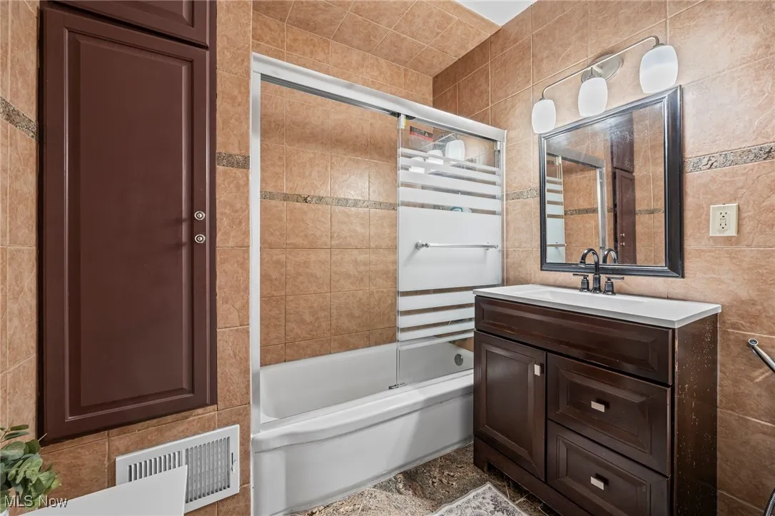 Bathroom featuring tile walls, enclosed tub / shower combo, and vanity