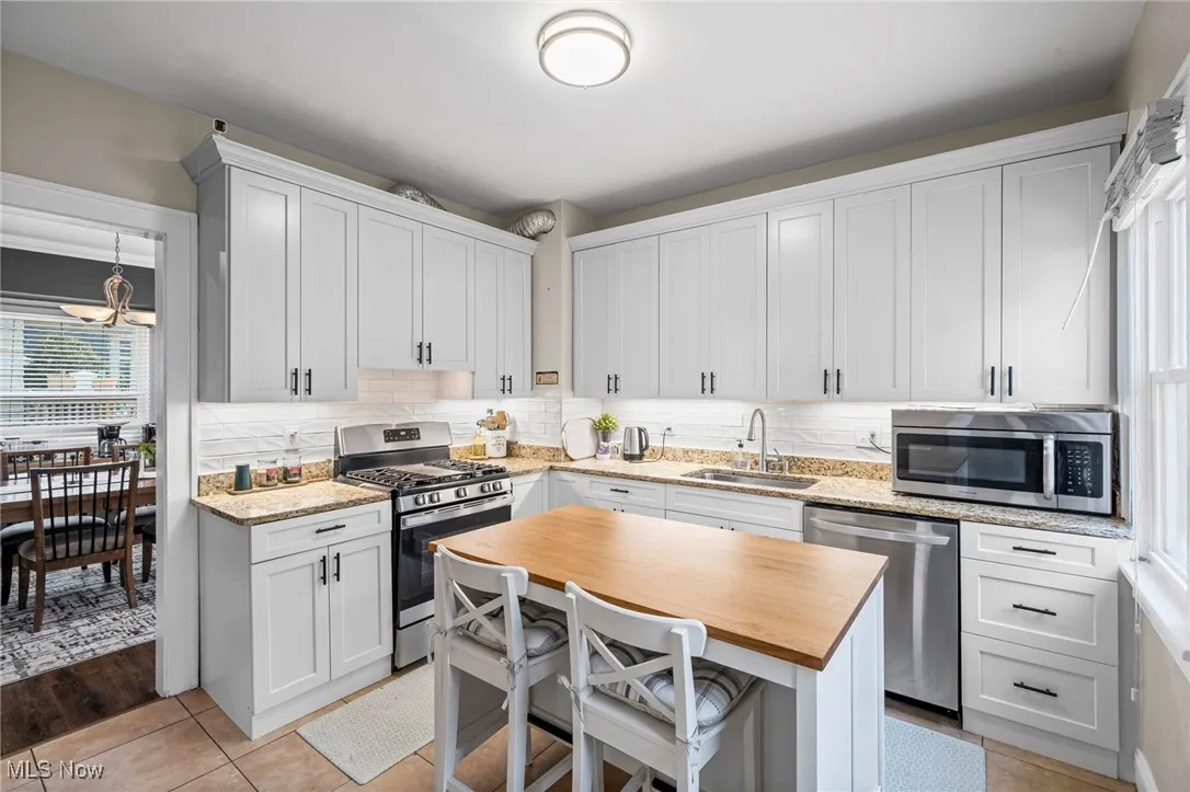Kitchen with stainless steel appliances, wood counters, a chandelier, backsplash, and white cabinets