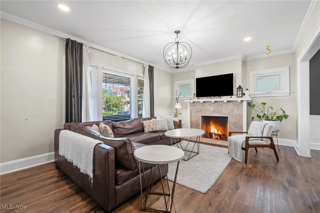 Living area featuring a fireplace with flush hearth, crown molding, dark wood finished floors, recessed lighting, and a chandelier