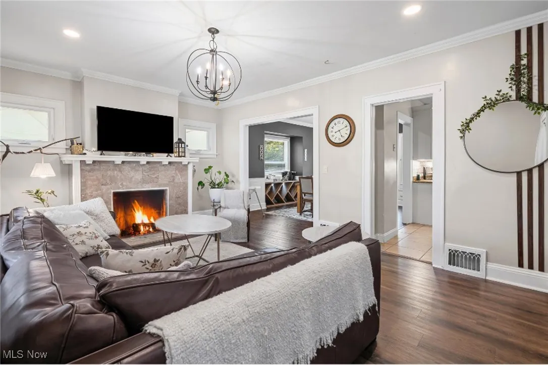 Living room featuring a tiled fireplace, wood finished floors, recessed lighting, a chandelier, and ornamental molding