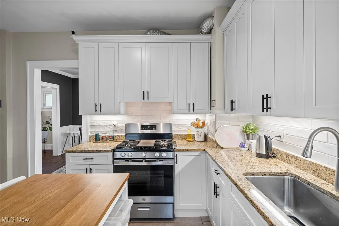 Kitchen featuring stainless steel range with gas stovetop, white cabinets, decorative backsplash, and light stone countertops