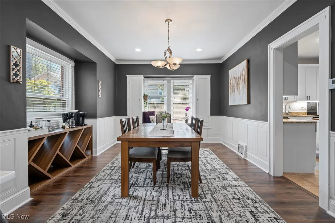 Dining area with plenty of natural light, a chandelier, dark wood-style floors, a wainscoted wall, and crown molding