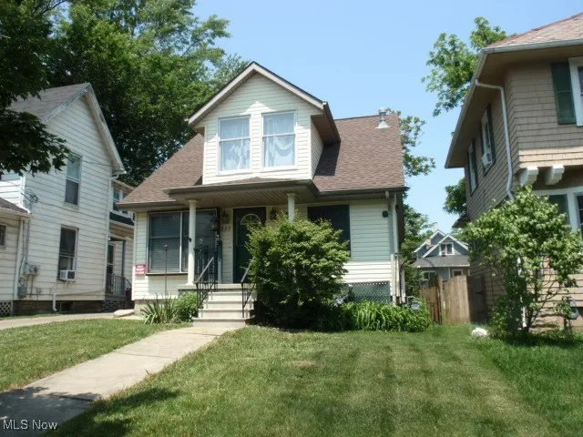 View of front of home with a front yard, roof with shingles, covered porch, and cooling unit