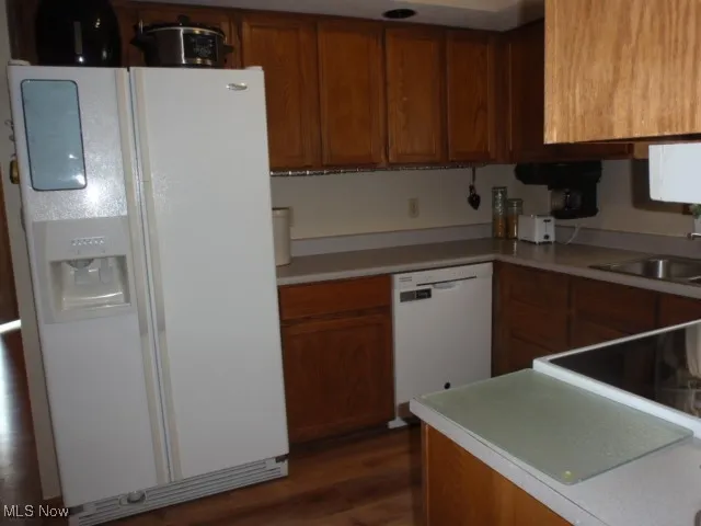 Kitchen with white appliances, brown cabinetry, wood finished floors, and light countertops