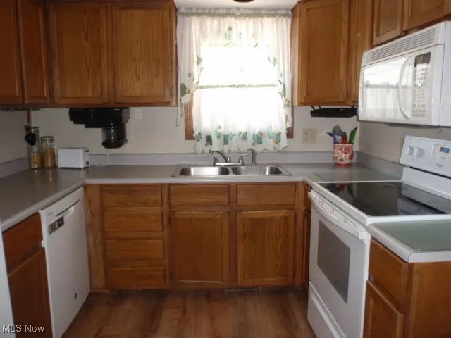 Kitchen with white appliances, light countertops, brown cabinets, and dark wood finished floors