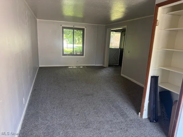 Unfurnished room with dark carpet, plenty of natural light, and a textured ceiling