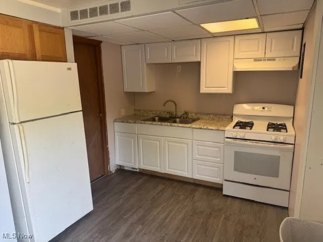 Kitchen with white appliances, under cabinet range hood, a paneled ceiling, dark wood-style floors, and white cabinets