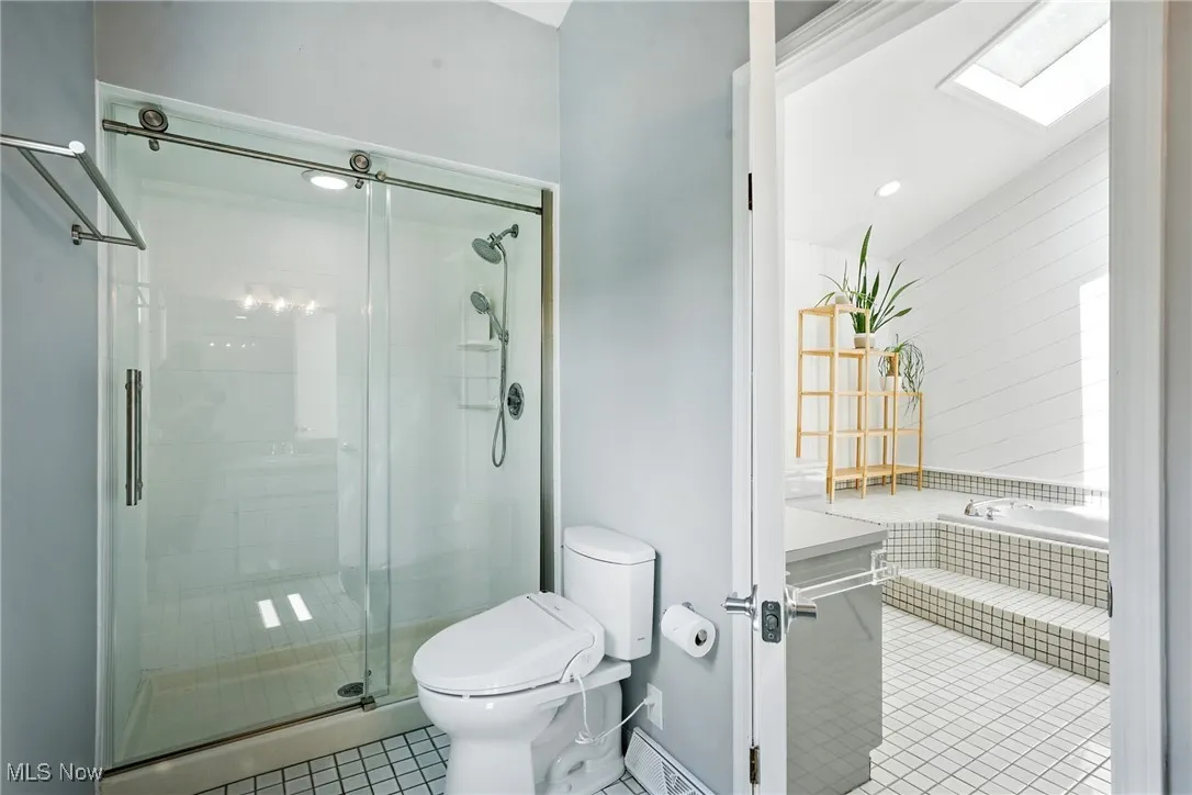 Full bath featuring tile patterned flooring, a skylight, a stall shower, and tiled tub