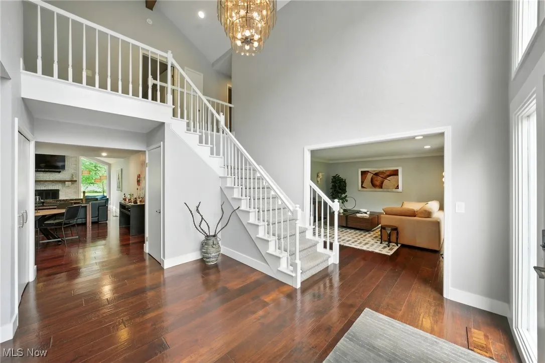 Entryway featuring high vaulted ceiling, stairway, wood-type flooring, a fireplace, and a chandelier