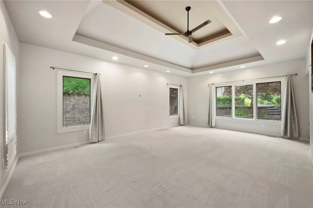 Carpeted first floor primary suite featuring a tray ceiling, plenty of natural light, recessed lighting, and a ceiling fan