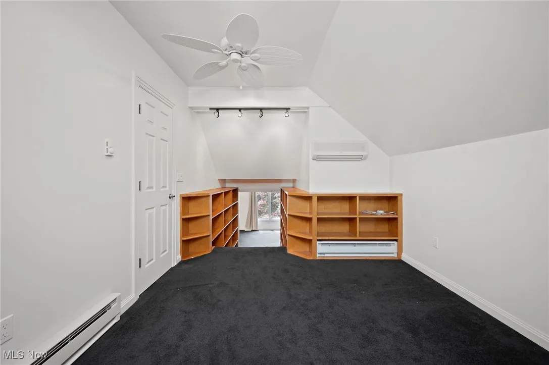 Additional storage, closet or loft space with baseboard heating, a baseboard radiator, vaulted ceiling, a wall unit AC, and a ceiling fan