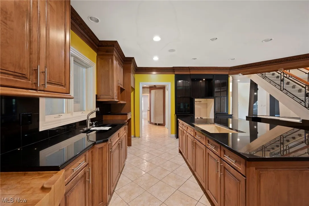 Kitchen featuring light tile patterned floors, crown molding, recessed lighting, brown cabinetry, and a large island with sink