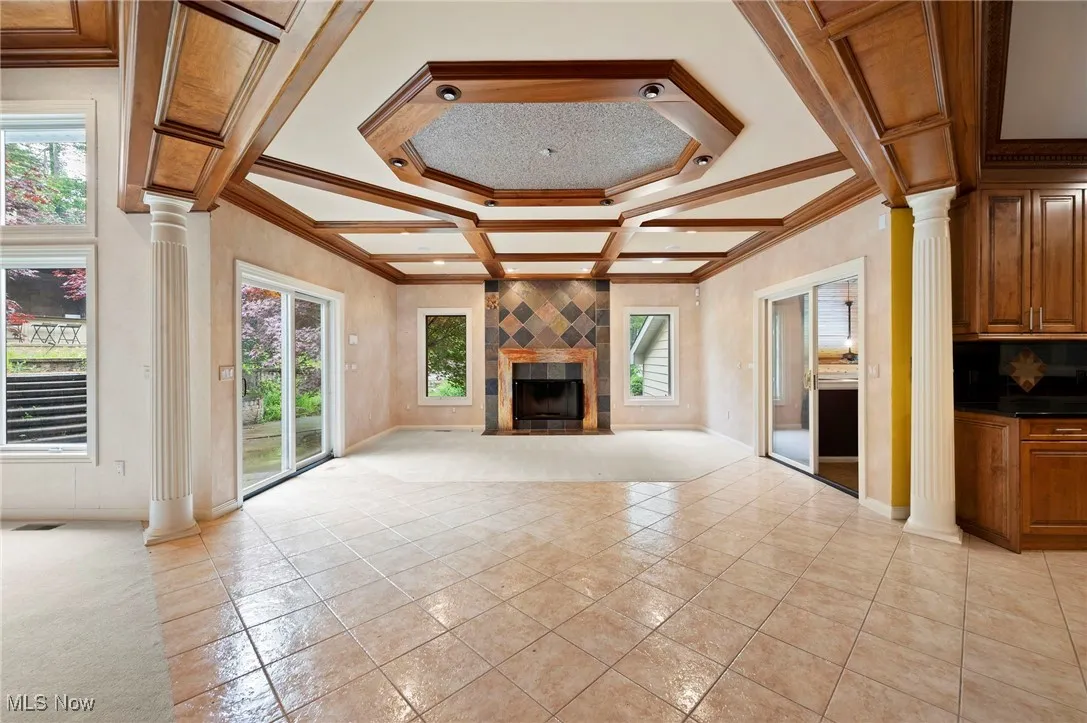 Unfurnished living room with ornate columns, coffered ceiling, crown molding, a fireplace, and beam ceiling