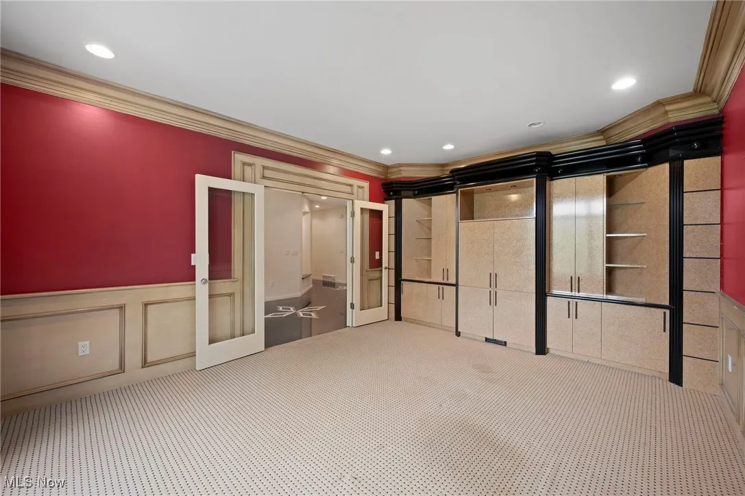 Unfurnished office with  decorative walls, crown molding, carpet, wainscoting, french doors and built-ins.
