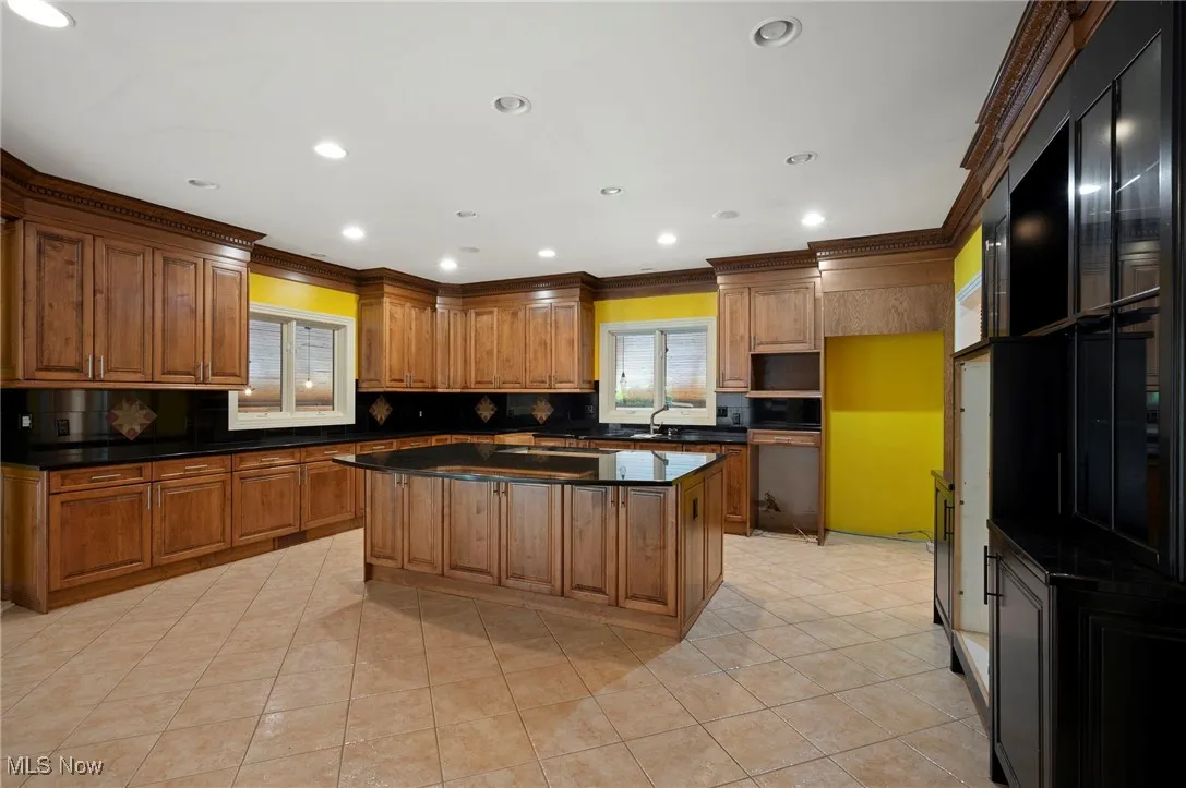 Kitchen with dark countertops, ornamental molding, backsplash, light tile patterned flooring, and a center island