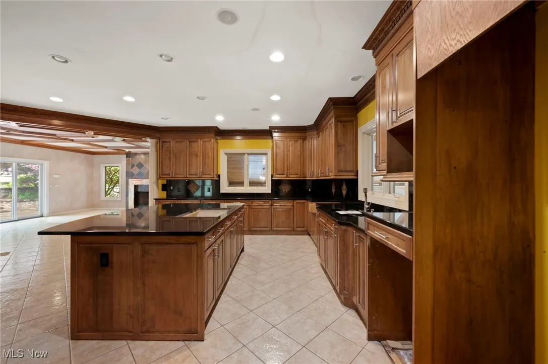 Kitchen with dark countertops, a kitchen island, backsplash, light tile patterned floors, and recessed lighting