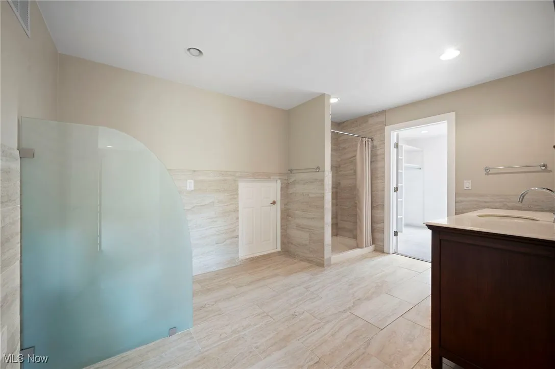 Bathroom with a stall shower, vanity, tile walls, and recessed lighting
