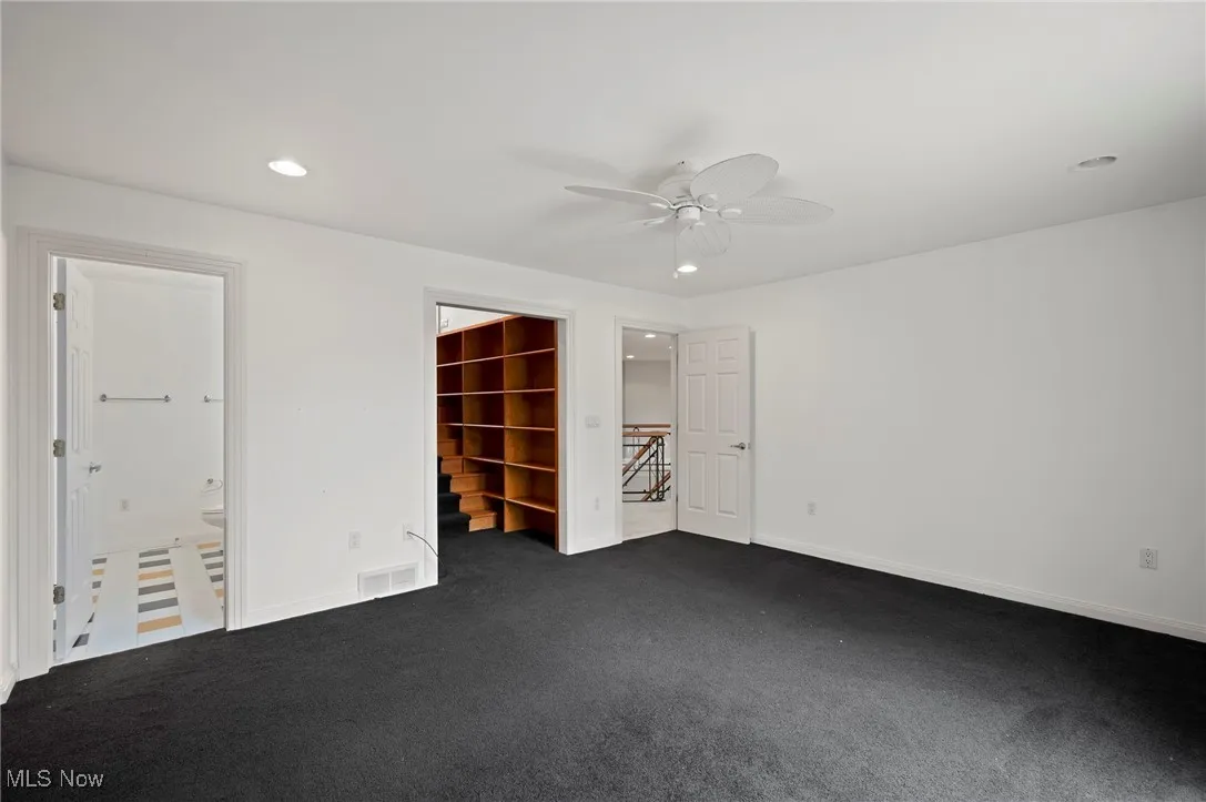 Unfurnished bedroom with dark carpet, recessed lighting, a spacious closet, a ceiling fan, and connected bathroom