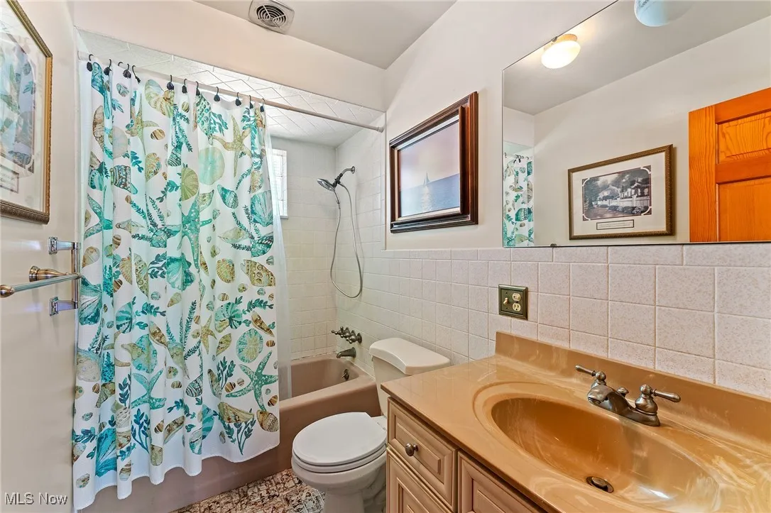 Bathroom with tile walls, vanity, and shower / bath combination with curtain