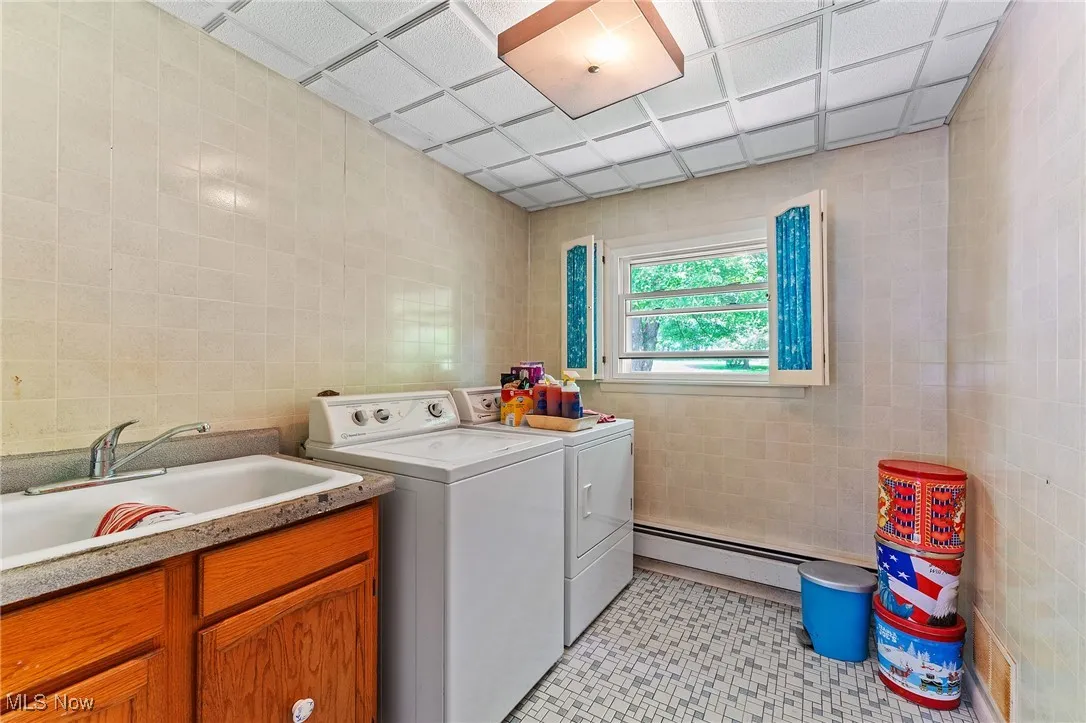 Laundry room featuring tile walls, washing machine and clothes dryer, a baseboard heating unit, and light tile patterned flooring