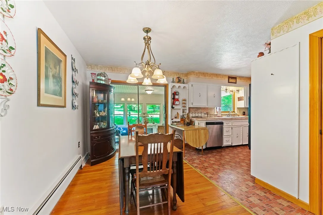 Dining room featuring a baseboard heating unit, light wood-style flooring, a chandelier, and a textured ceiling
