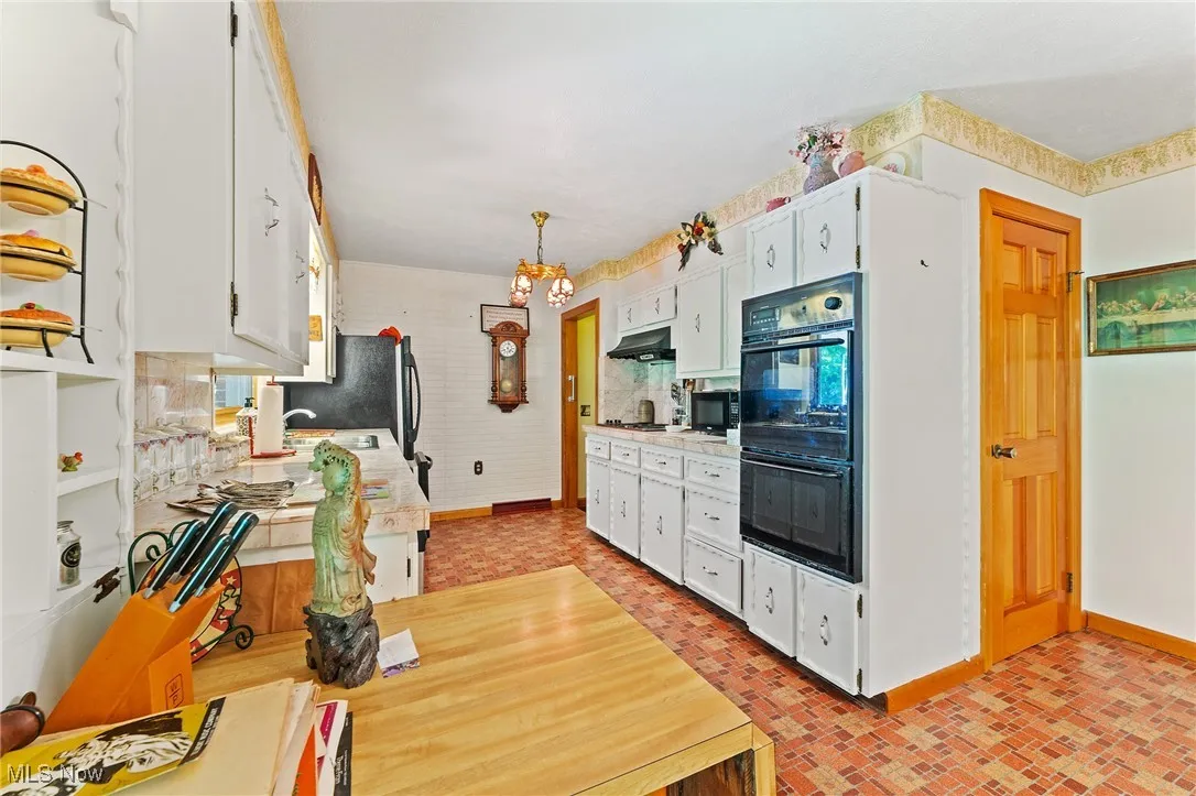 Kitchen with under cabinet range hood, brick patterned flooring, white cabinetry, light countertops, and a chandelier