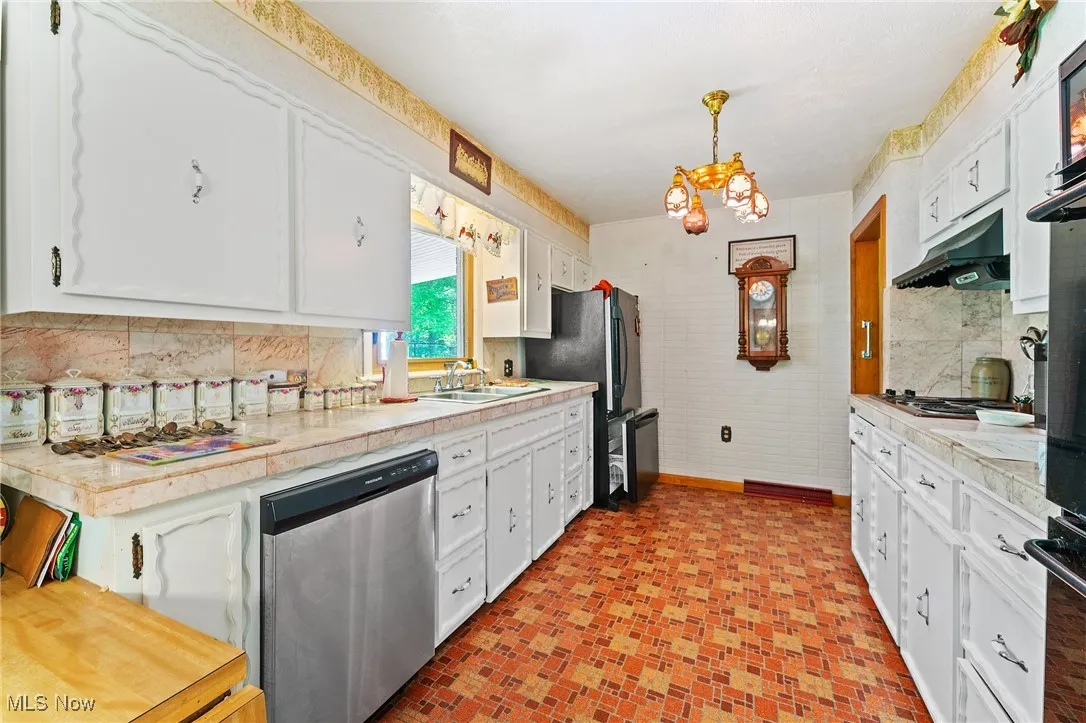 Kitchen featuring stainless steel appliances, under cabinet range hood, white cabinets, and a chandelier