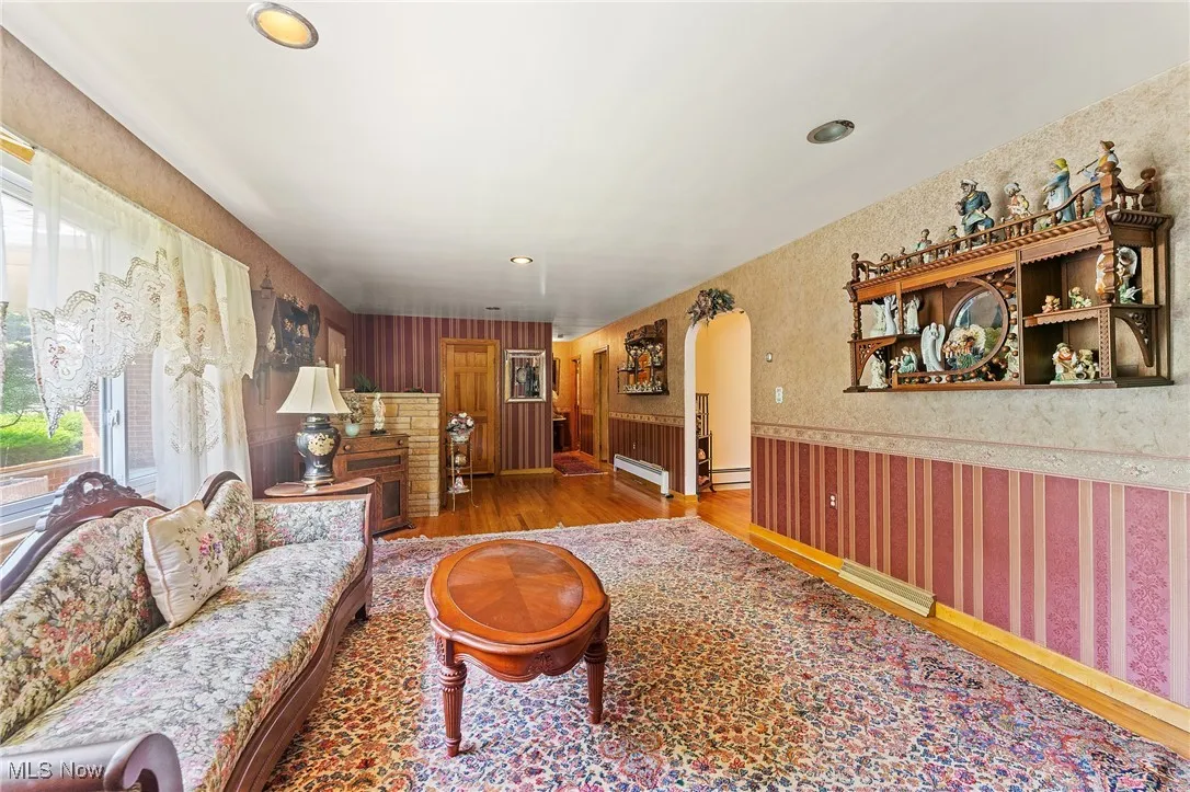 Living area featuring wallpapered walls, healthy amount of natural light, wood finished floors, arched doorway.