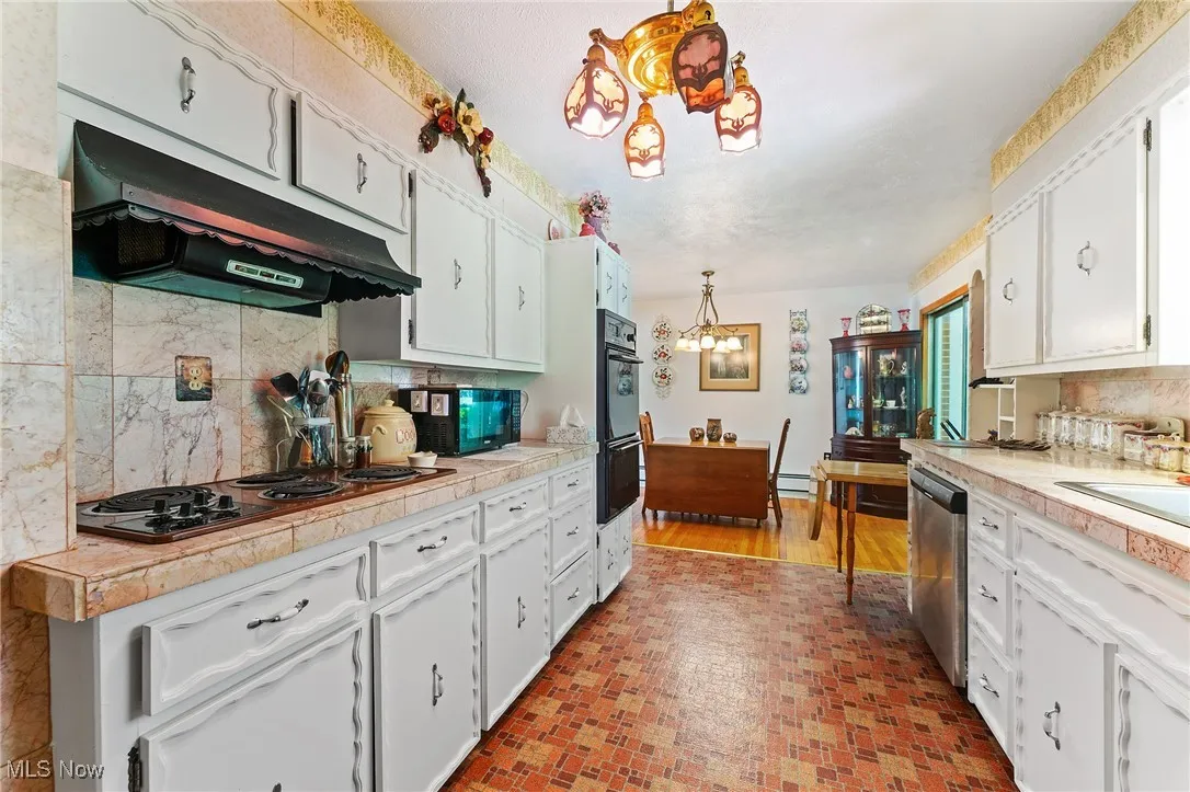 Kitchen featuring under cabinet range hood, a chandelier, black appliances, white cabinetry, and light countertops
