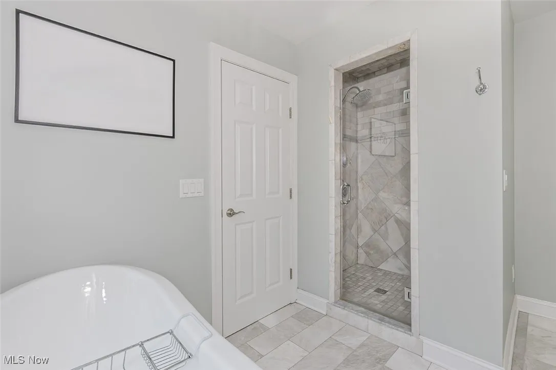 Primar bath with bathtub, dual vanity sink, marble tile, and walk-in shower.