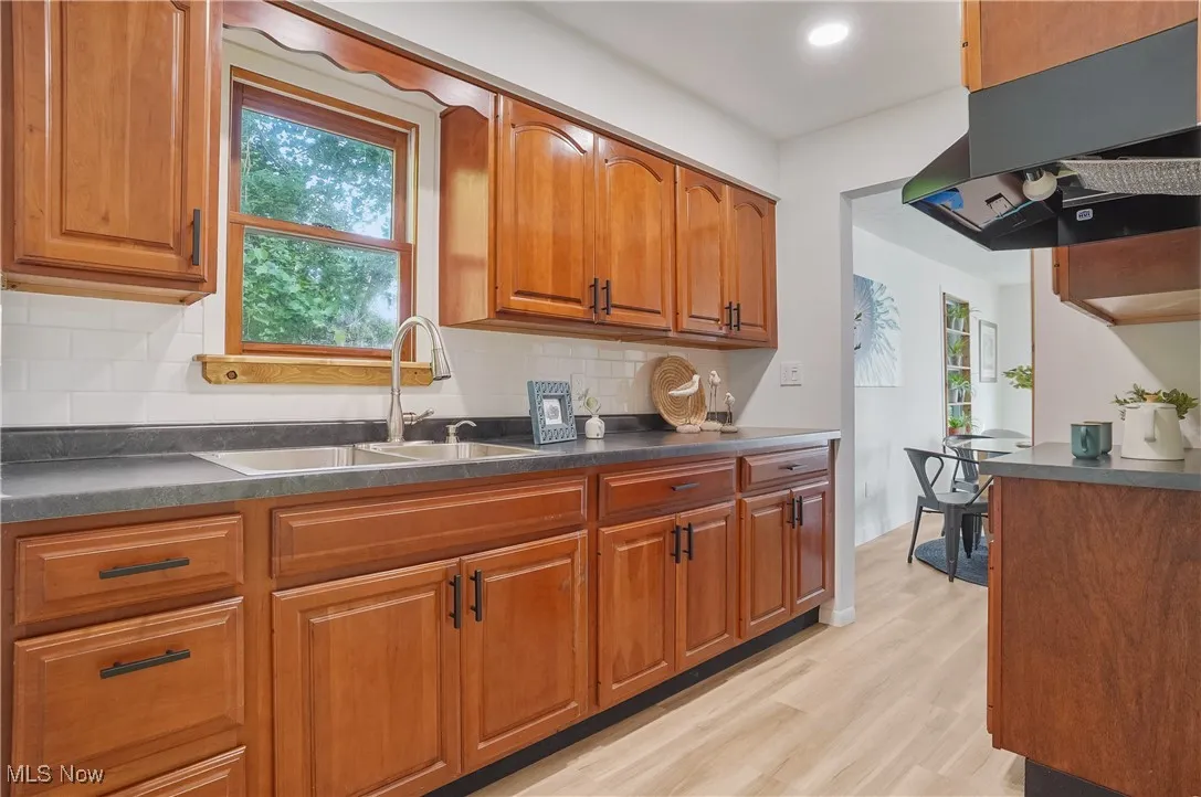 Kitchen with ventilation hood, dark countertops, brown cabinetry, light wood-style floors, and recessed lighting