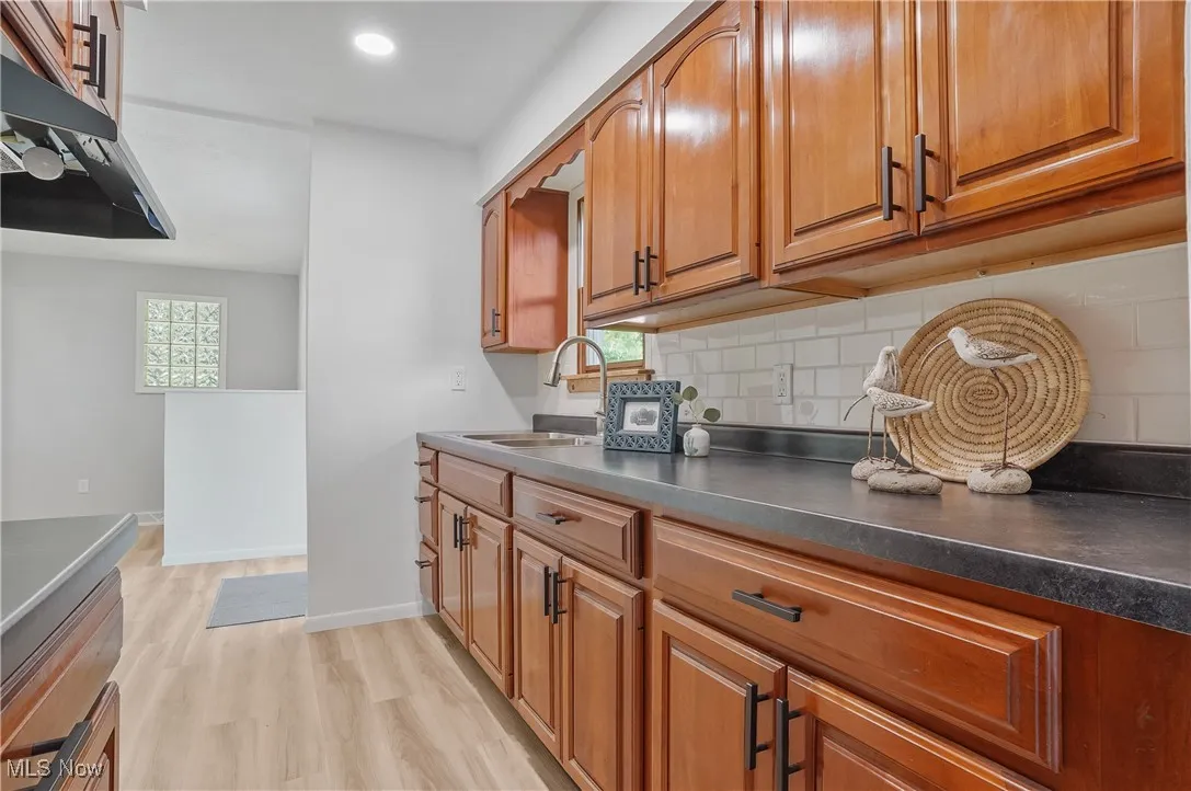 Kitchen featuring brown cabinets, tasteful backsplash, light wood-style flooring, dark countertops, and recessed lighting