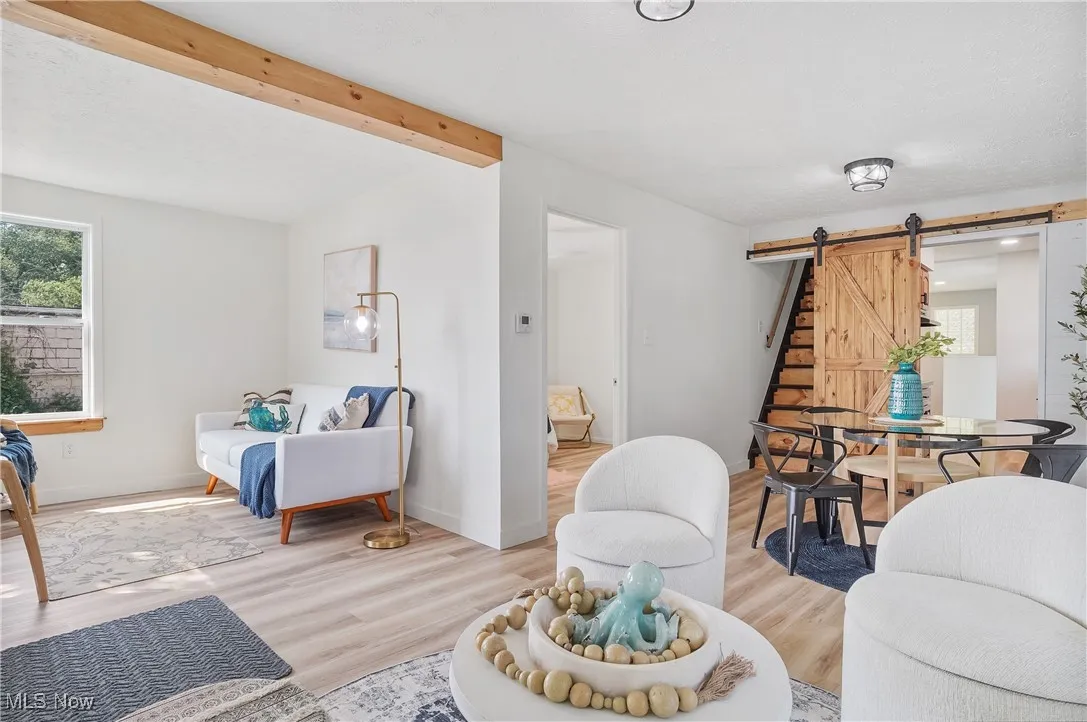 Living room featuring a barn door, light wood-type flooring, beam ceiling, and stairs