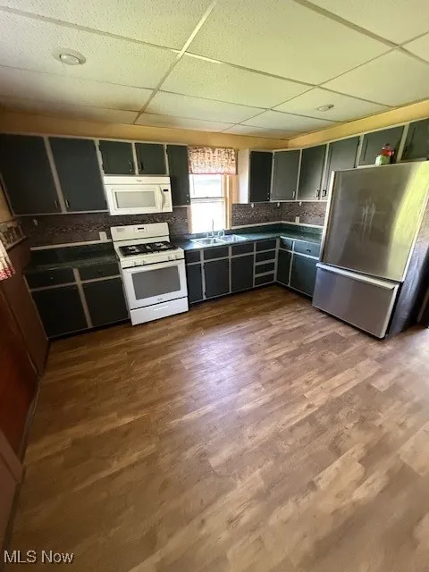 Kitchen with stove, fridge, dark countertops, a paneled ceiling, and tasteful backsplash