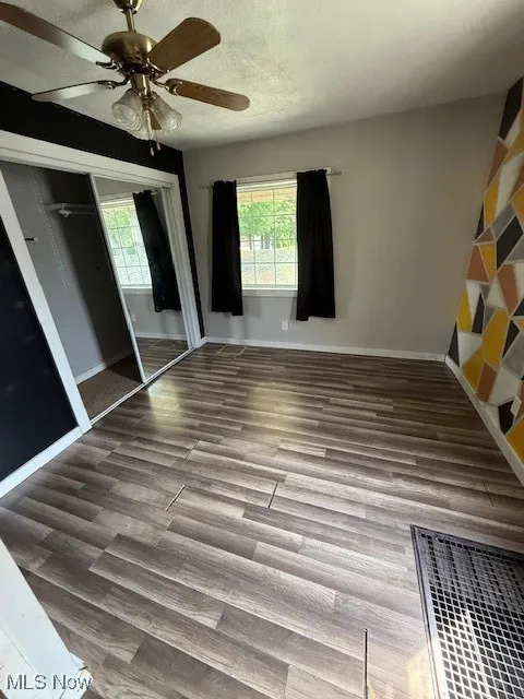 Unfurnished bedroom with multiple windows, wood finished floors, a closet, and ceiling fan
