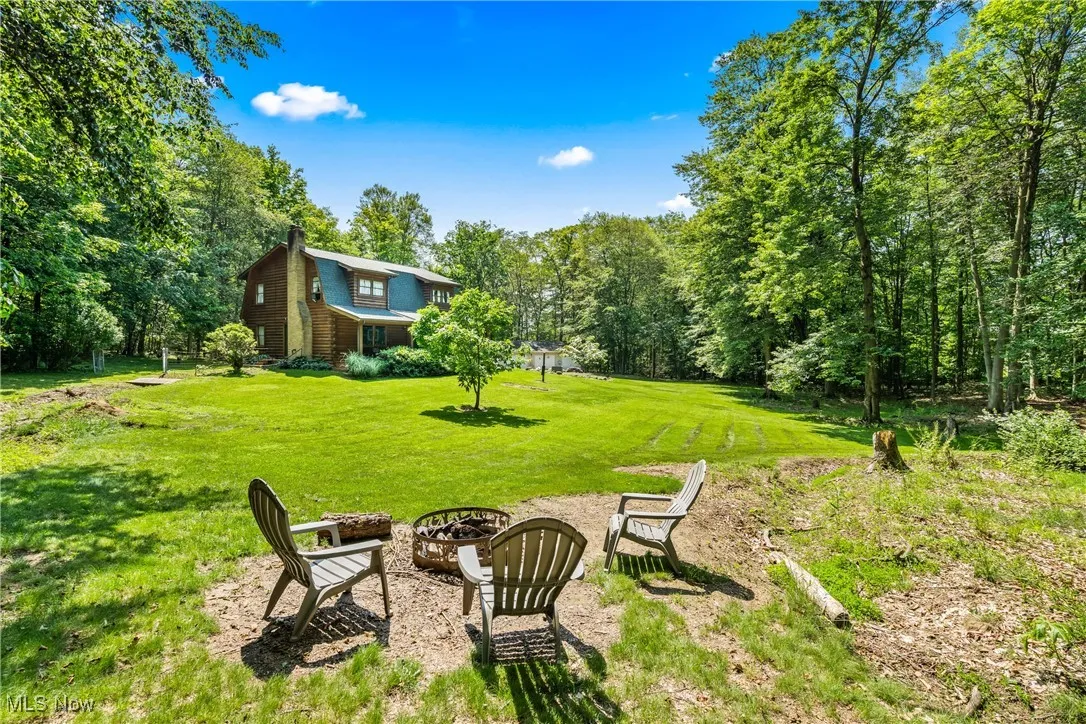 View of grassy yard featuring a fire pit and a view of trees