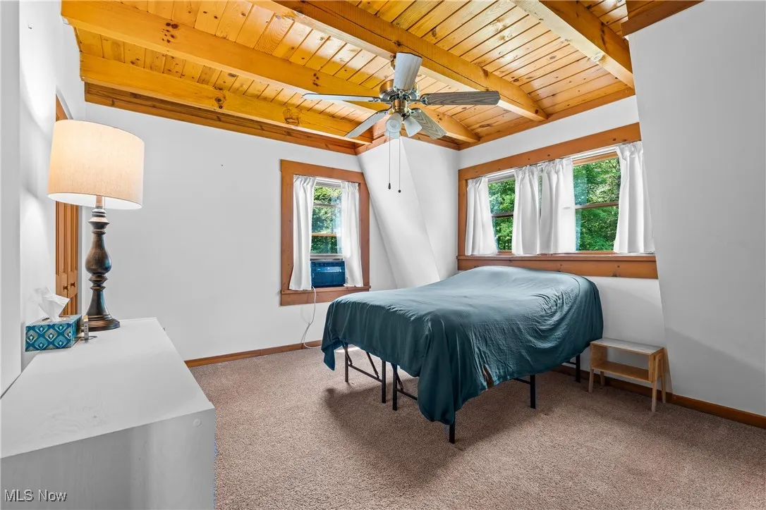 Carpeted bedroom featuring a wooden ceiling with exposed beams and a ceiling fan