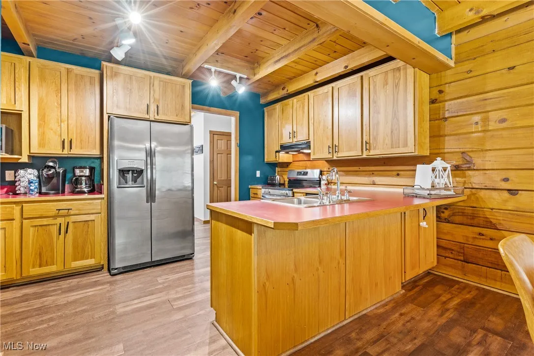 Kitchen featuring stainless steel appliances, a wood ceiling with exposed beams, under cabinet range hood, light wood-type flooring, and a kitchen bar