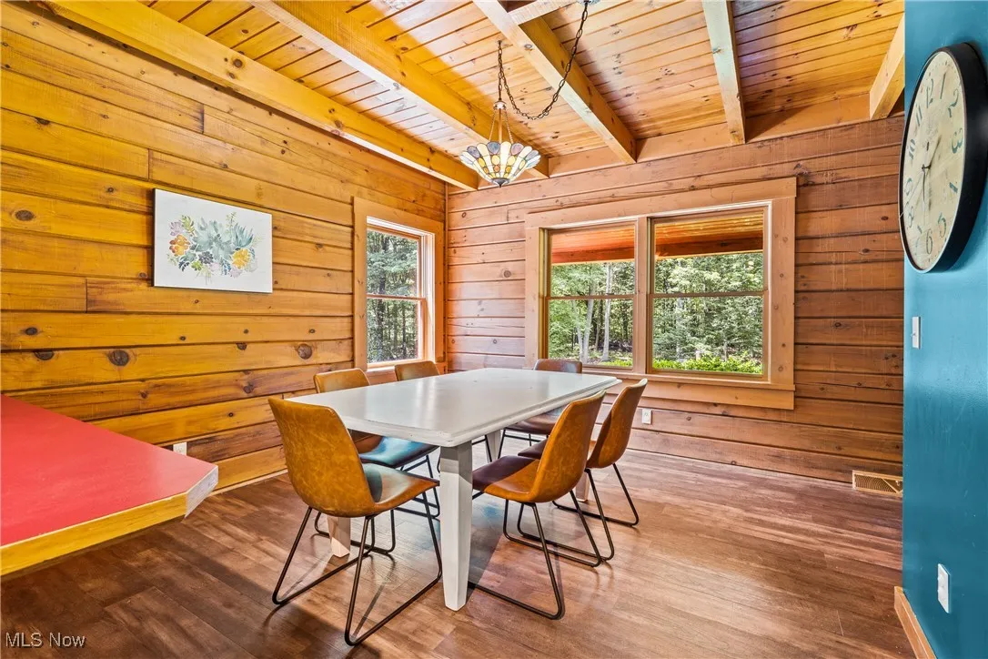 Dining area featuring a wood ceiling with exposed beams, wooden walls, wood finished floors, and a chandelier