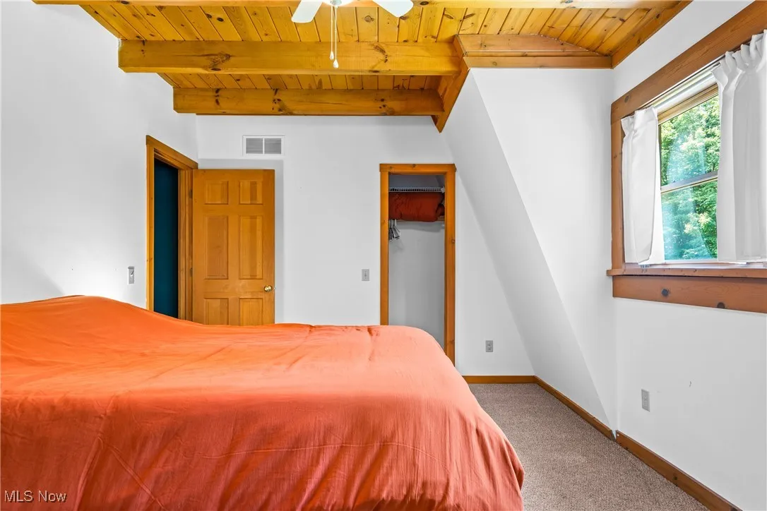 Bedroom with a wood ceiling with exposed beams and carpet