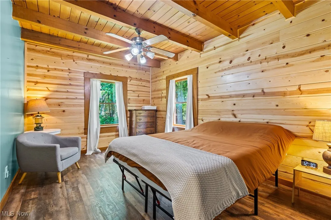 Bedroom with wood finished floors, a wood ceiling with exposed beams, and wooden walls