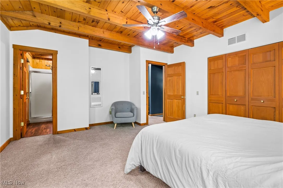 Carpeted bedroom featuring a wooden ceiling with exposed beams, a closet, and a ceiling fan