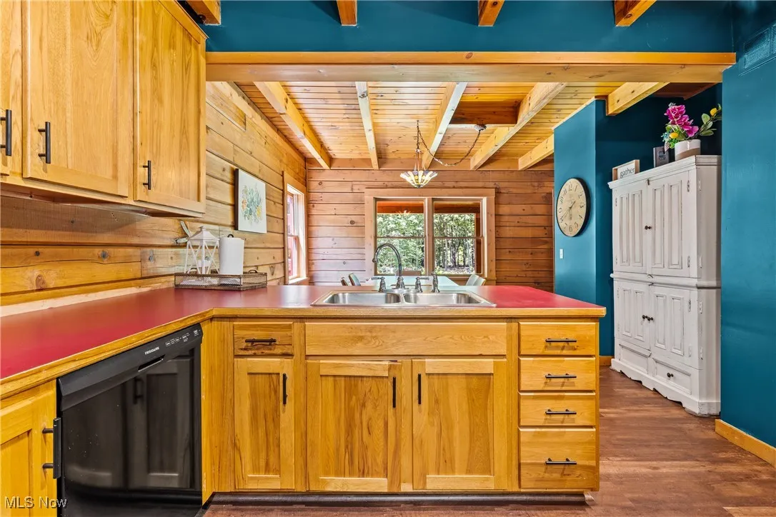 Kitchen with black dishwasher, a wood ceiling with exposed beams, a peninsula, wood walls, and wood finished floors