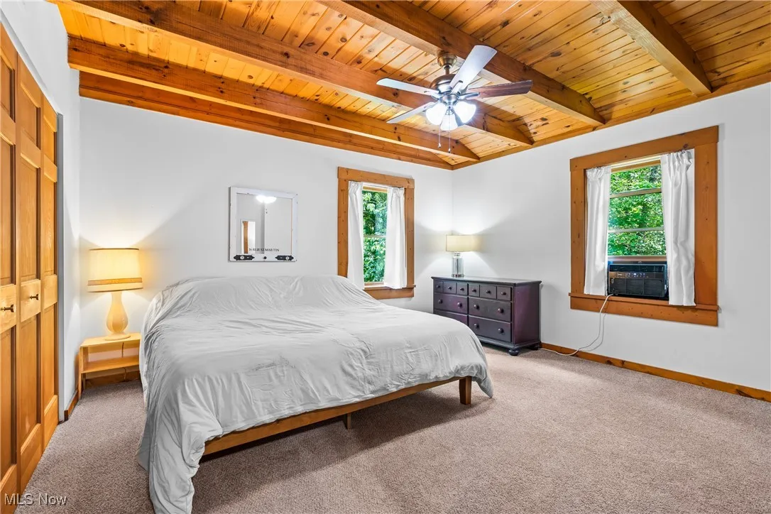 Carpeted bedroom with a wooden ceiling with exposed beams, multiple windows, cooling unit, and a ceiling fan
