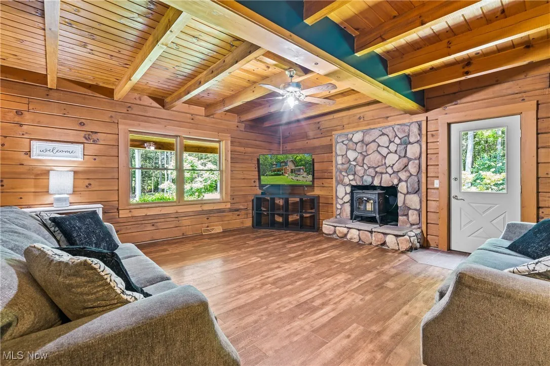 Living area with a wooden ceiling with exposed beams, wood walls, wood finished floors, and ceiling fan